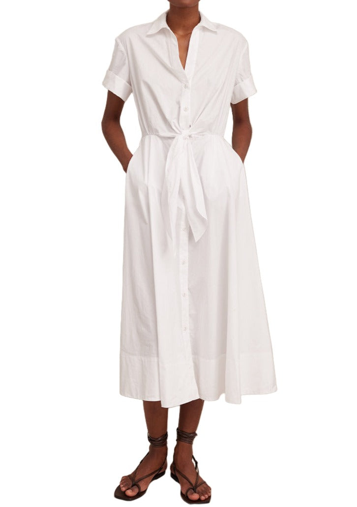 A person stands against a plain background wearing the Cara Cara Asbury Dress, designed by Cara Cara. The white cotton poplin dress features a self-tie waist, effortlessly showcasing a chic and timeless look.