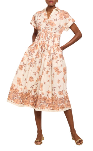 A person wearing the Cara Cara Nash Midi Dress—a light-colored, fit and flare shirt dress with a brown floral pattern and functional pockets—paired with tan open-toe sandals.