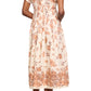 A person stands facing away, wearing the Cara Cara Nash Midi Dress—a light, fit and flare shirt dress with a brown floral pattern, pockets, and short sleeves—paired with flat sandals.