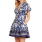 The woman is wearing a Cara Cara Nash Mini Dress, featuring short sleeves, a white and blue floral pattern, pintucks, functional pockets, a V-neck, and a flared skirt.