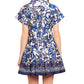 Back view of a woman in the Cara Cara Nash Mini Dress, a blue and white floral-patterned mini shirtdress with short sleeves, pintucks, and pleats.