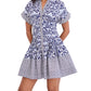 A woman wears the Cara Cara Nash Mini Dress—a fit-and-flare mini shirtdress with short sleeves, a collar, side seam pockets, and a blue and white geometric floral pattern.