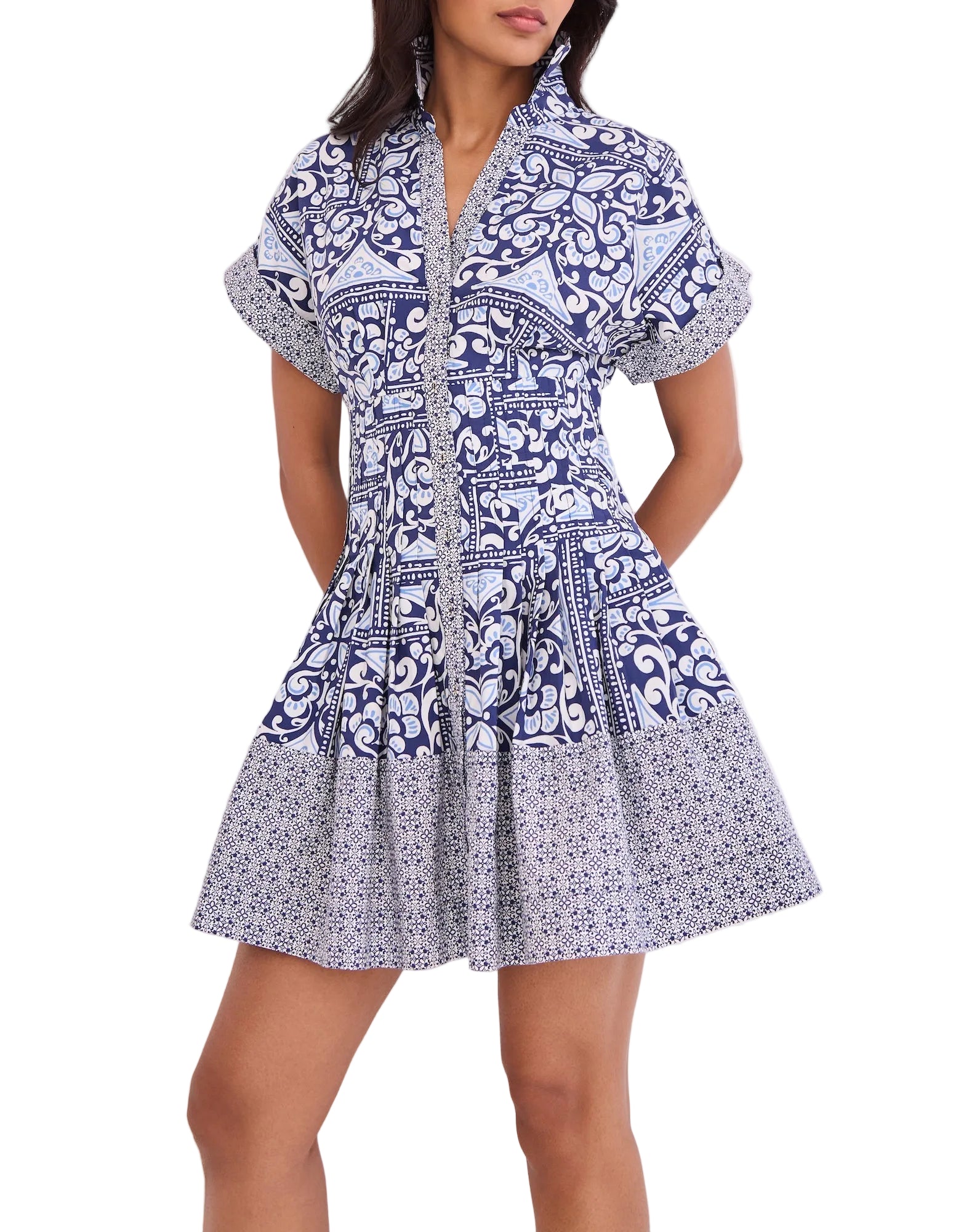 A woman wears the Cara Cara Nash Mini Dress—a fit-and-flare mini shirtdress with short sleeves, a collar, side seam pockets, and a blue and white geometric floral pattern.
