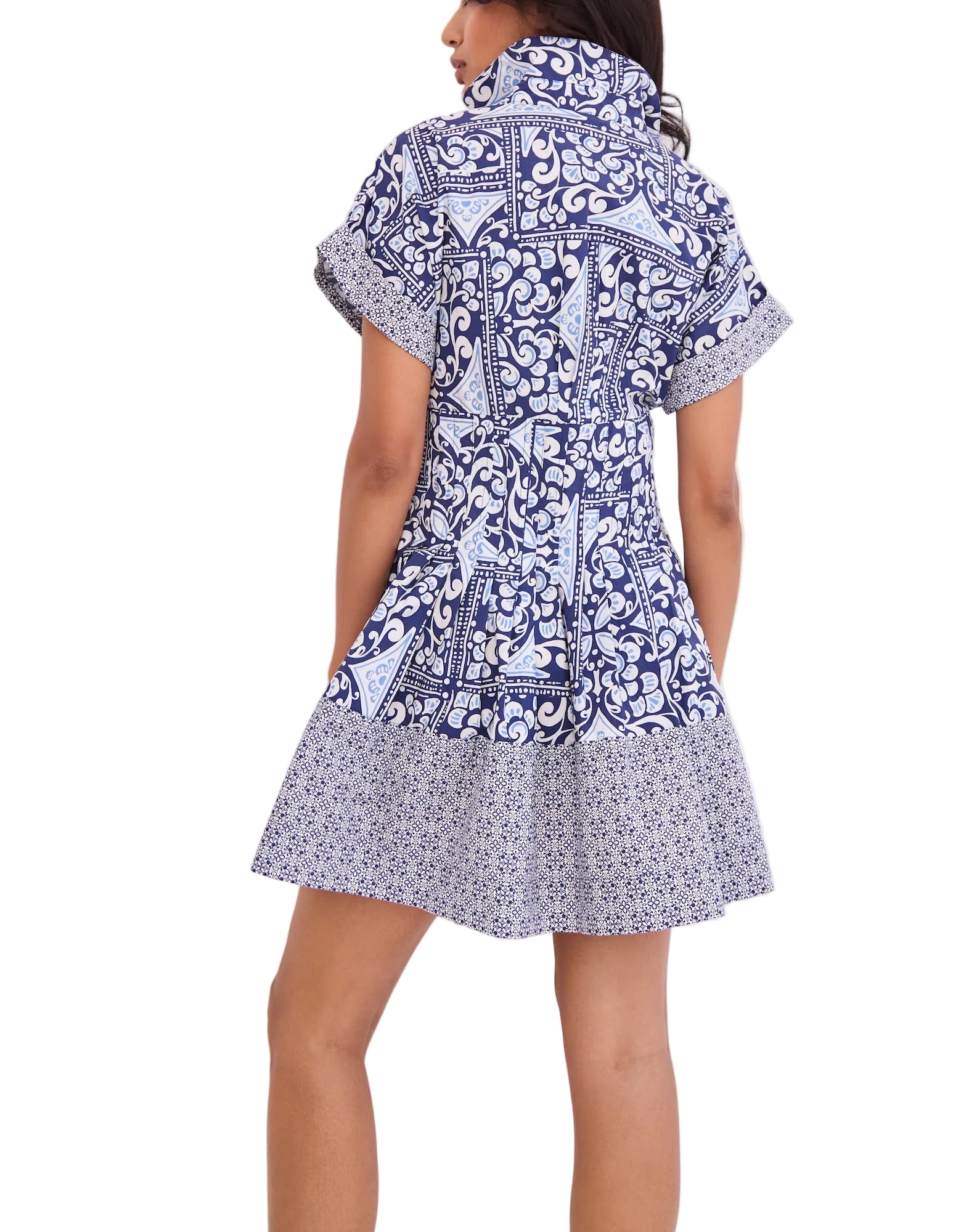 A person stands with their back to the camera against a plain background, wearing the Cara Cara Nash Mini Dress—a short, blue and white fit-and-flare style featuring short sleeves and side seam pockets.