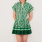 A person wearing the Cara Cara Nash Mini Dress—a short-sleeved, collared green and white patterned mini shirtdress with a pleated skirt—stands against a plain light background.