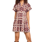 A woman wearing the Cara Cara Nash Mini Dress—a short-sleeve, knee-length fit-and-flare dress with a red and brown floral pattern—stands with hands in pockets, paired with brown knee-high boots.