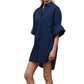 A person wearing the Staud Nico Dress, a loose-fitting navy blue cotton poplin mini shirtdress with short sleeves, stands against a plain white background.