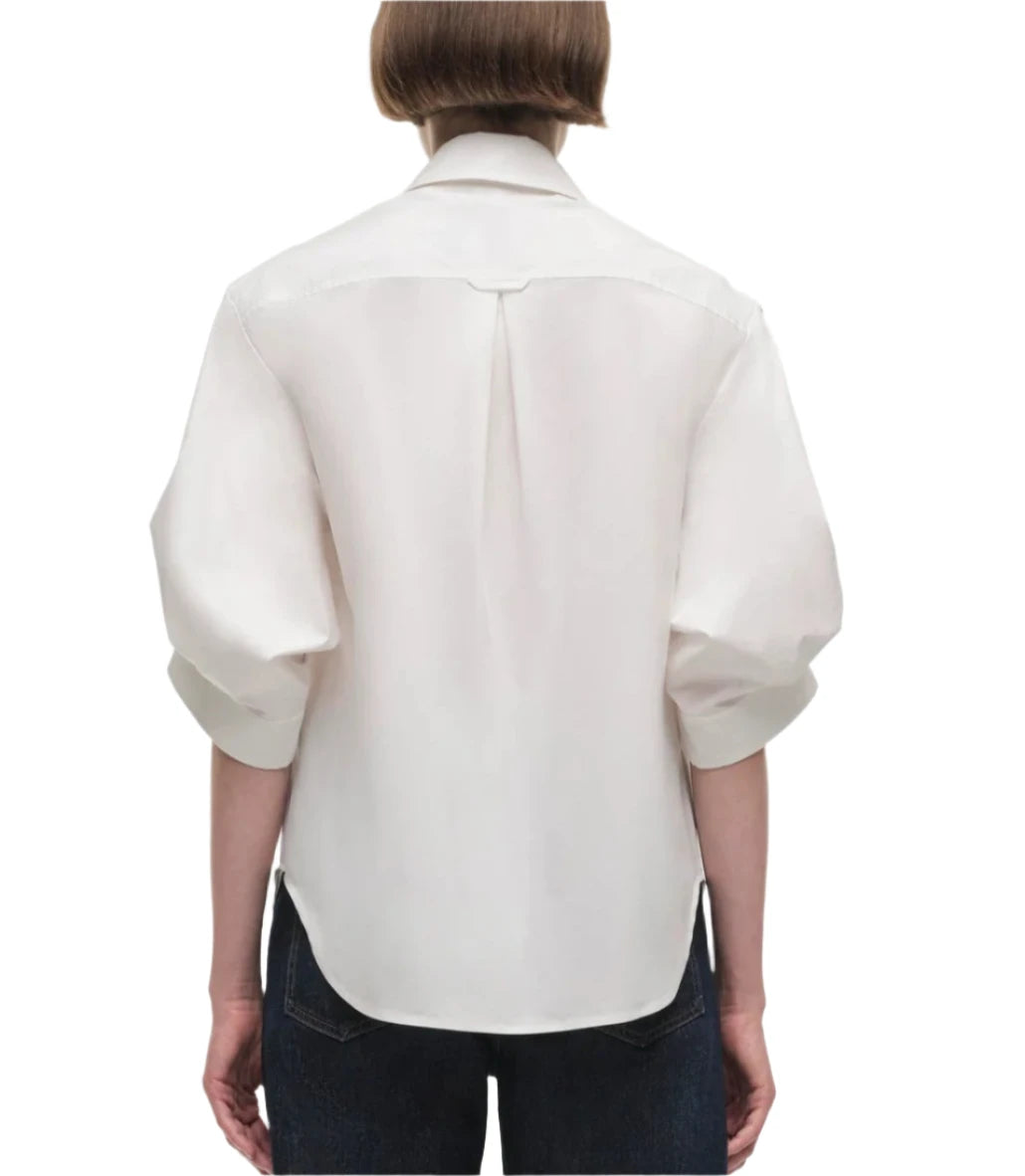 A person wearing the Simkhai Gemma Shirt, a tailored-fit blouse, with rolled-up cuffs and black pants, viewed from the back.