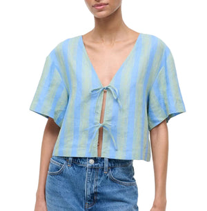 A person wearing the Staud Ava Linen Top—a short-sleeve, blue and green striped V-neck with an adjustable tie front—paired with blue jeans.