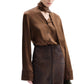 Model wearing CO's Scarf Blouse in brown silk with a tie collar and long wide cuffs, paired with a dark brown skirt, set against a white background.