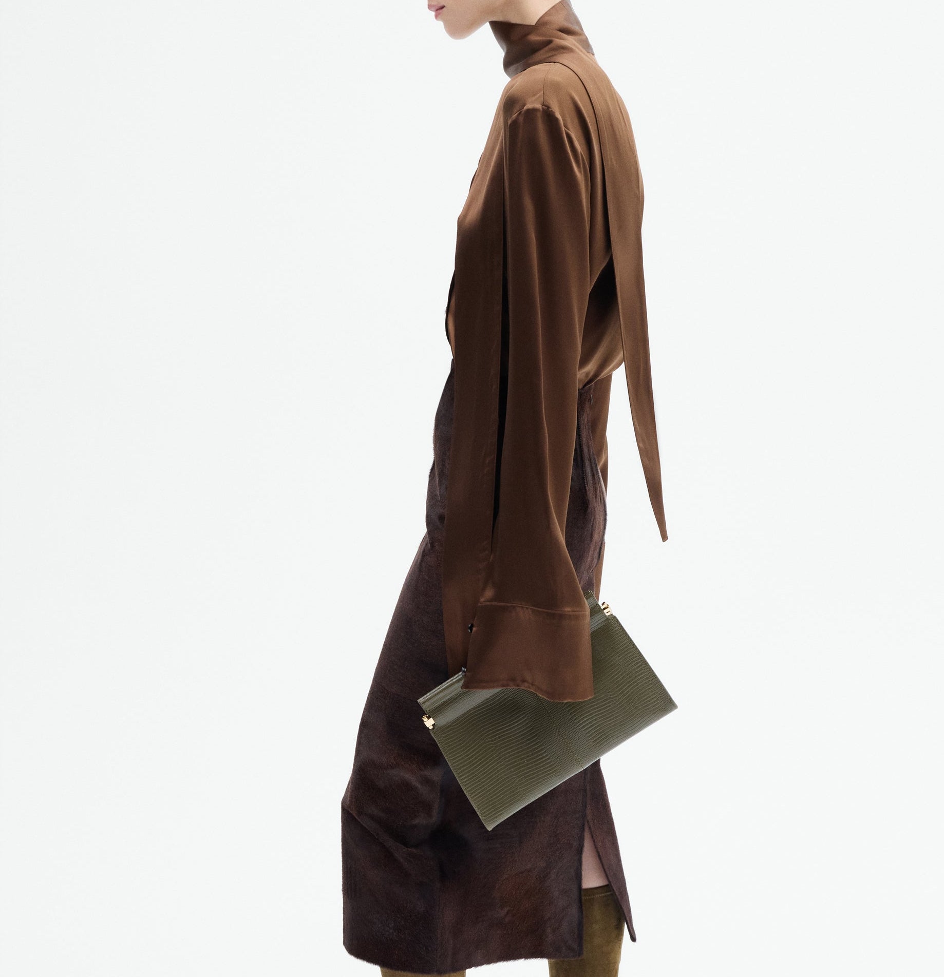 Person in a CO Scarf Blouse and matching skirt, holding a textured green clutch bag, photographed from the side against a white background.
