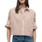 A woman wears the TWP Next Ex Stripe Shirt—a brown and white Italian cotton top with rolled sleeves and a boxy silhouette—paired with blue jeans.