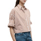 A person wearing the TWP Next Ex Stripe Shirt in brown and white vertical stripes with rolled-up sleeves and blue jeans, shown from mid-torso up.
