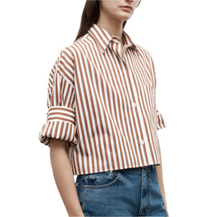 A person wearing the TWP Next Ex Stripe Shirt in brown and white vertical stripes with rolled-up sleeves and blue jeans, shown from mid-torso up.