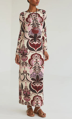 A woman wears the Cara Cara Danae Midi Dress with bold red and pink patterns, paired with flat sandals and a statement necklace.