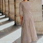 A woman stands on a sunlit stone walkway in chic workwear—a Lela Rose Striped Cotton Dolman Sleeve Top styled as a dress with open-toed heels—columns rising elegantly in the background.