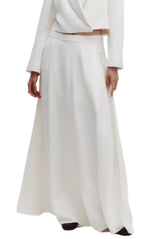 A person wearing the TWP Cecelias Skirt, a long white high-waisted maxi, paired with a matching white long-sleeve top and black shoes.
