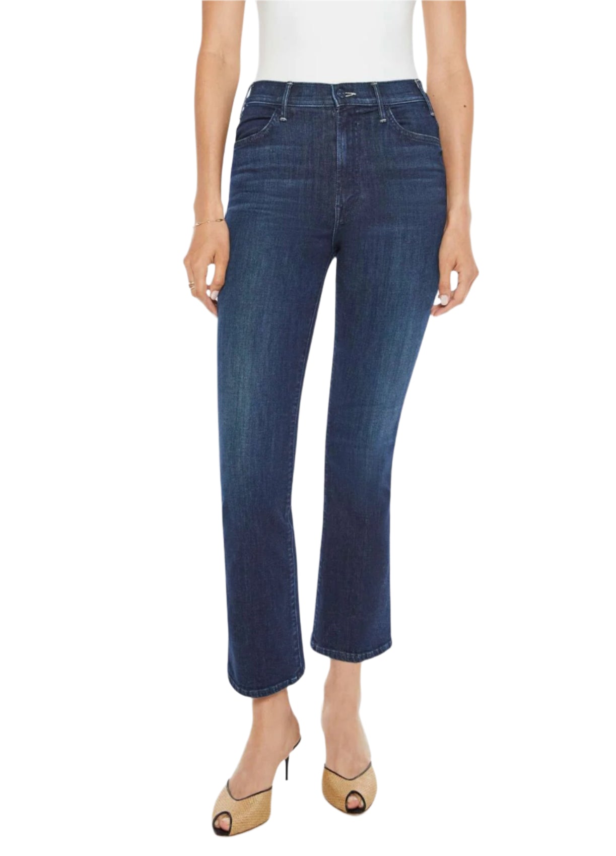 A person wears Mother Denim The Hustler Ankle jeans by Mother in dark blue with a high-rise skinny flare and ankle-length inseam, complemented by open-toe heels, standing against a plain background.