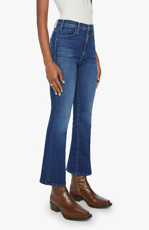 A person wearing Mother’s The Hustler Ankle blue high-rise skinny-flare jeans, a white top, and brown ankle boots stands against a plain background.