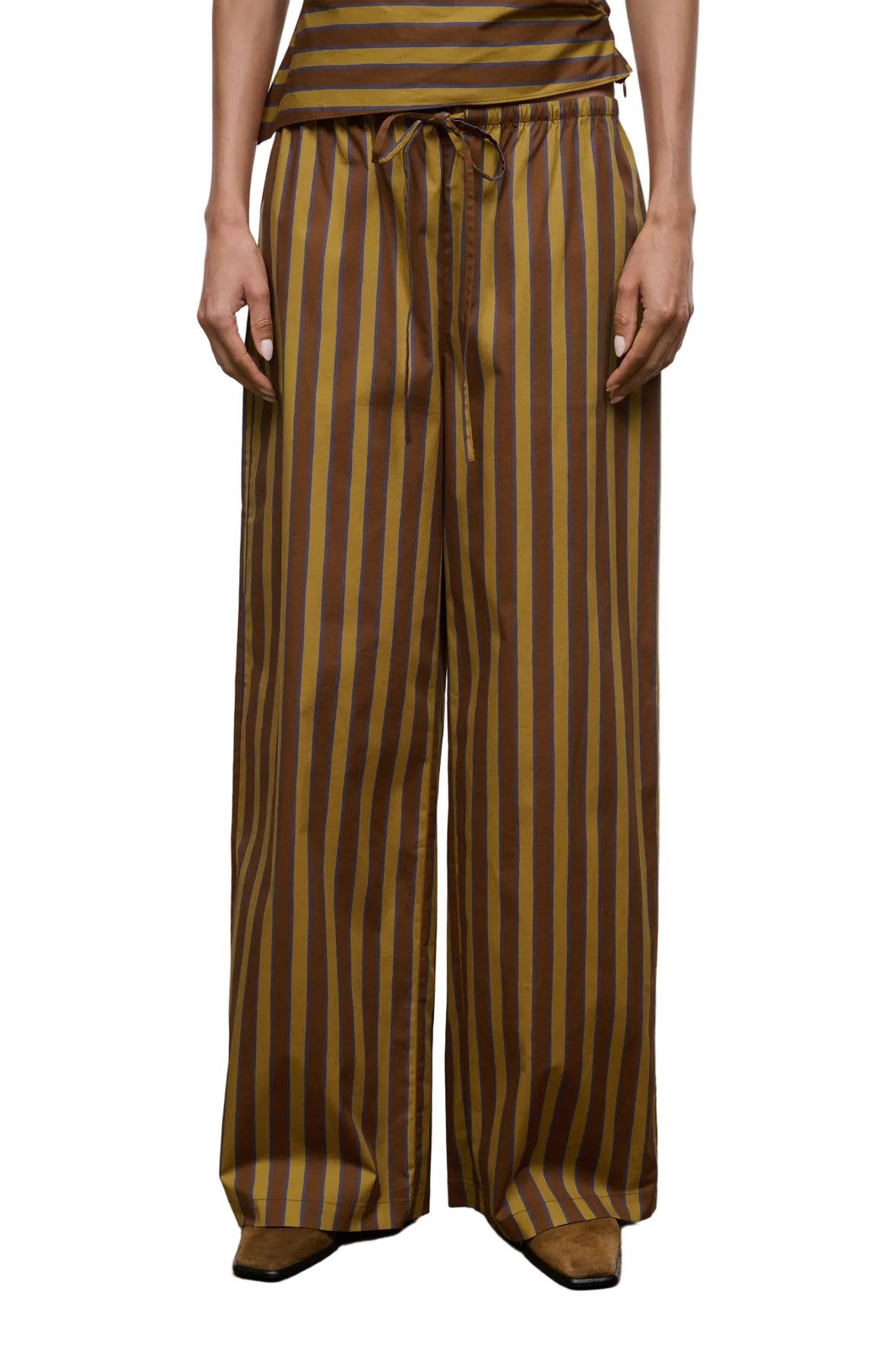 A person wearing the Staud Mateo Cotton Poplin Pant, featuring a mid-rise fit, drawstring waist, and brown and yellow vertical stripes in wide-leg cotton poplin, stands against a plain background.