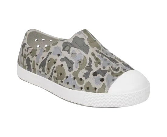 The Kids’ Jefferson Print Shoes by Native Shoes feature a slip-on design with a green and gray camouflage pattern, a white toe cap, perforated sides, and a shock-absorbent Sugarlite white rubber sole.