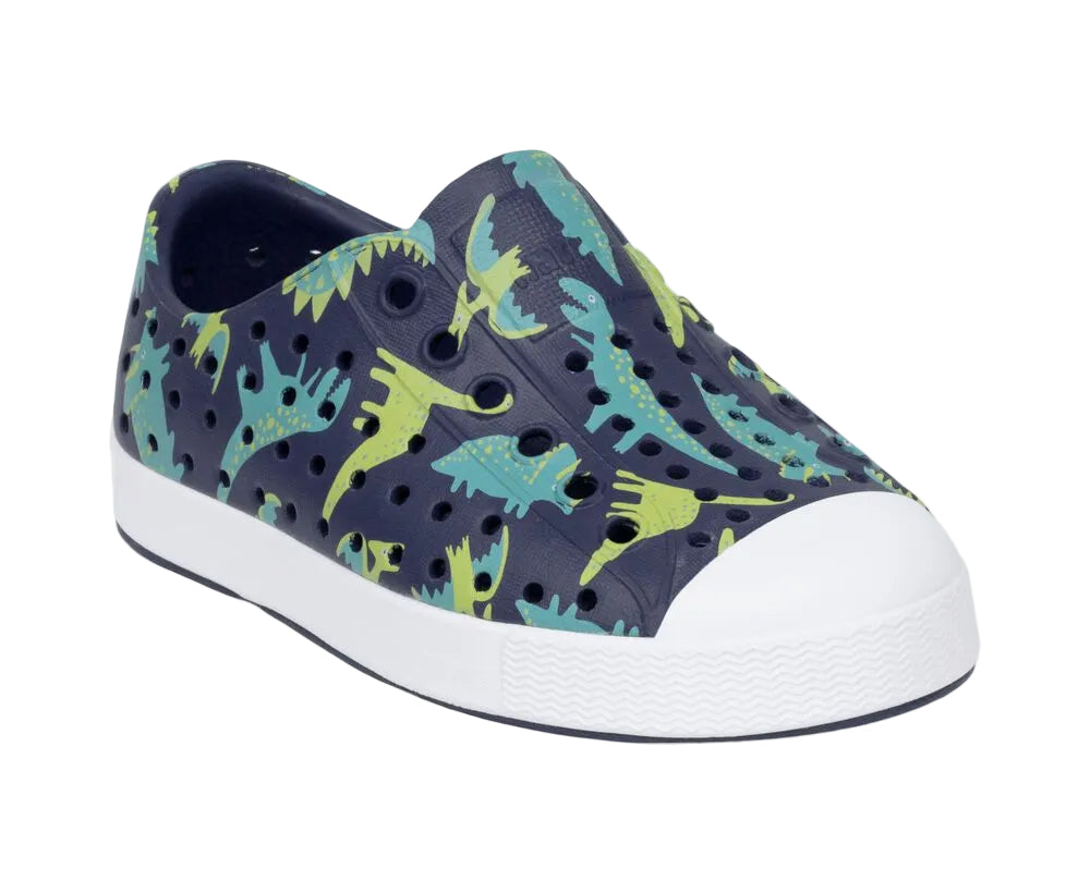 The Kids’ Jefferson Print Shoes from Native Shoes feature a navy slip-on design with a white toe cap, perforated holes, and an eye-catching green and blue dinosaur print on the upper. Made with shock-absorbent Sugarlite™ material, these shoes offer all-day comfort and durability.
