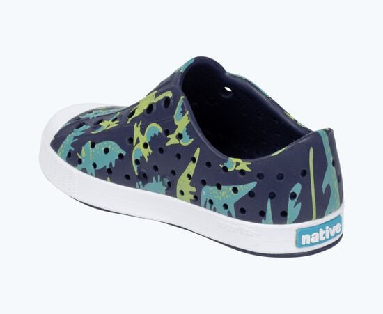The Kids’ Jefferson Print Shoes by Native Shoes feature a playful blue, green, and yellow dinosaur print, convenient slip-on design, ventilation holes for breathability, a shock-absorbent white Sugarlite sole, and the “native” logo on the heel.