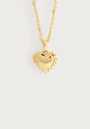 The Anabel Aram Heart Locket Necklace features a puffy, gold-dipped brass heart pendant with small round accents, creating a charming keepsake locket displayed on a plain white background.