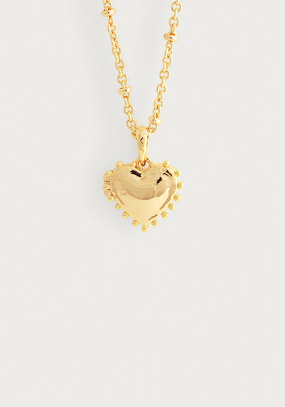 The Anabel Aram Heart Locket Necklace features a puffy, gold-dipped brass heart pendant with small round accents, creating a charming keepsake locket displayed on a plain white background.