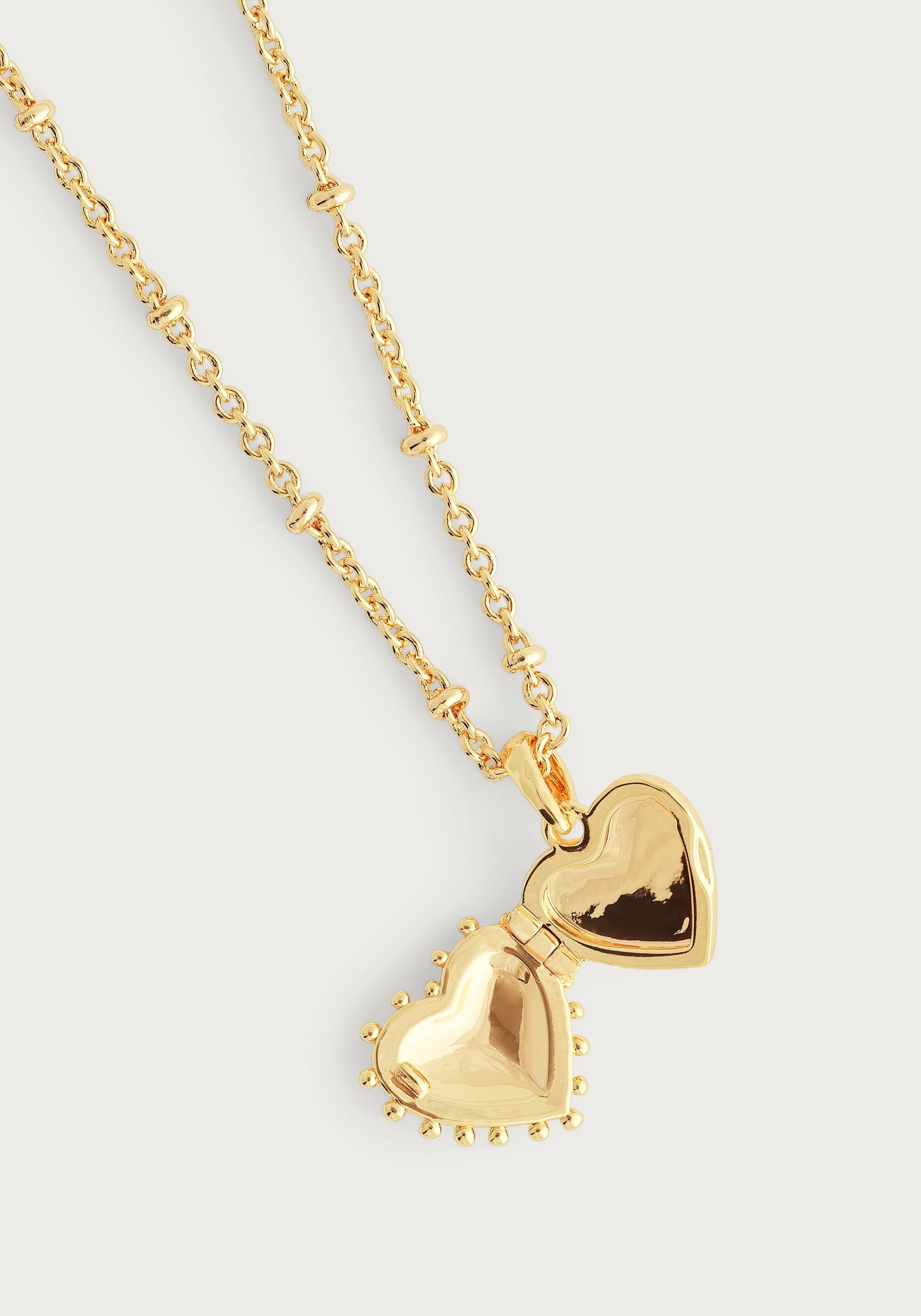The Anabel Aram Heart Locket Necklace features gold dipped brass and a beaded chain, opening to reveal two hollow heart halves—a timeless keepsake for your cherished memories.