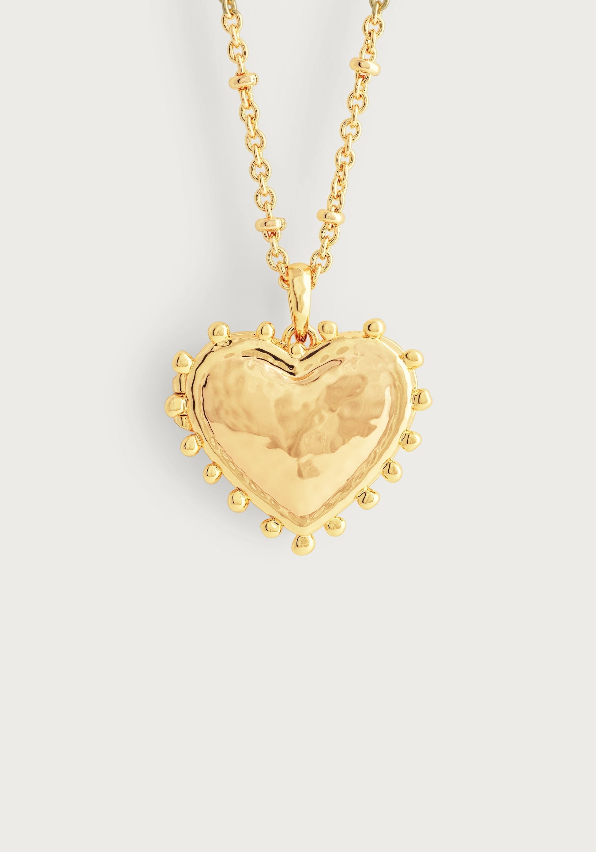 The Anabel Aram Heart Locket Necklace features a gold dipped brass, heart-shaped pendant with textured details around the edge, creating a timeless keepsake shown against a plain white background.