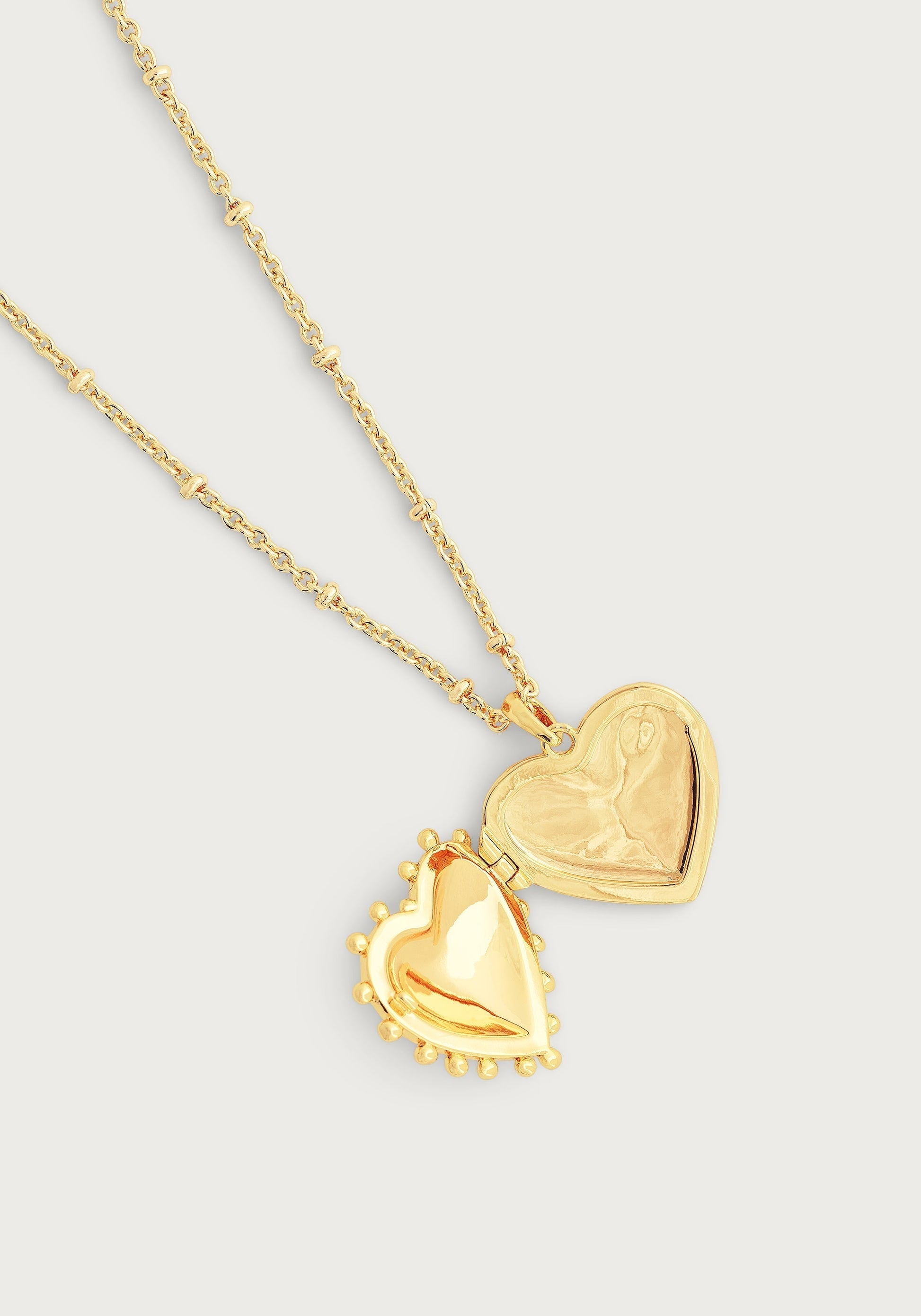 The Anabel Aram Heart Locket Necklace, crafted from gold-dipped brass with a beaded-edge detail, is an elegant keepsake shown on a simple light background.