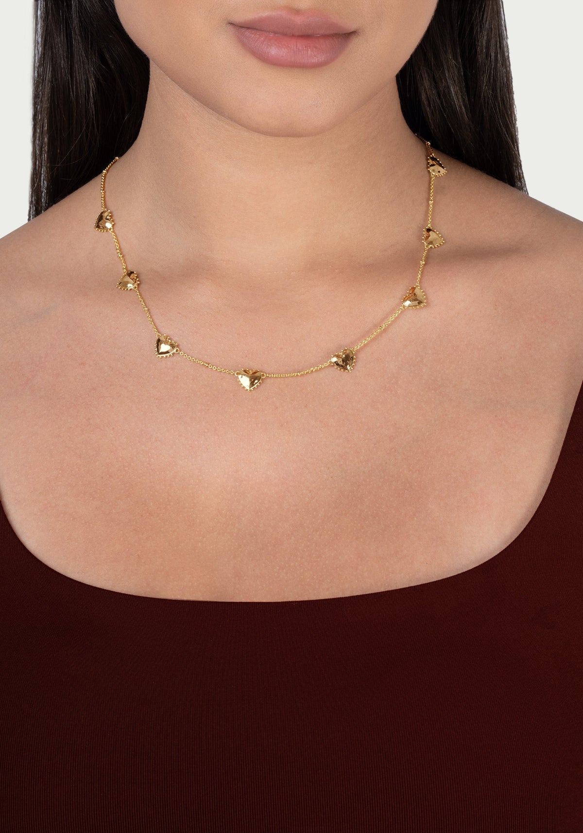 Anabel Aram Heart Station Necklace featuring a delicate 18k gold plated chain with evenly spaced, small puffy hearts worn around a person’s neck.