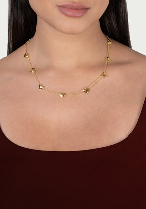 Anabel Aram Heart Station Necklace featuring a delicate 18k gold plated chain with evenly spaced, small puffy hearts worn around a person’s neck.