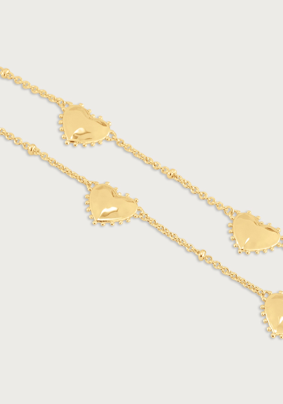 Anabel Aram Heart Station Necklace featuring an 18k gold plated chain with evenly spaced puffy heart charms with beaded edges.