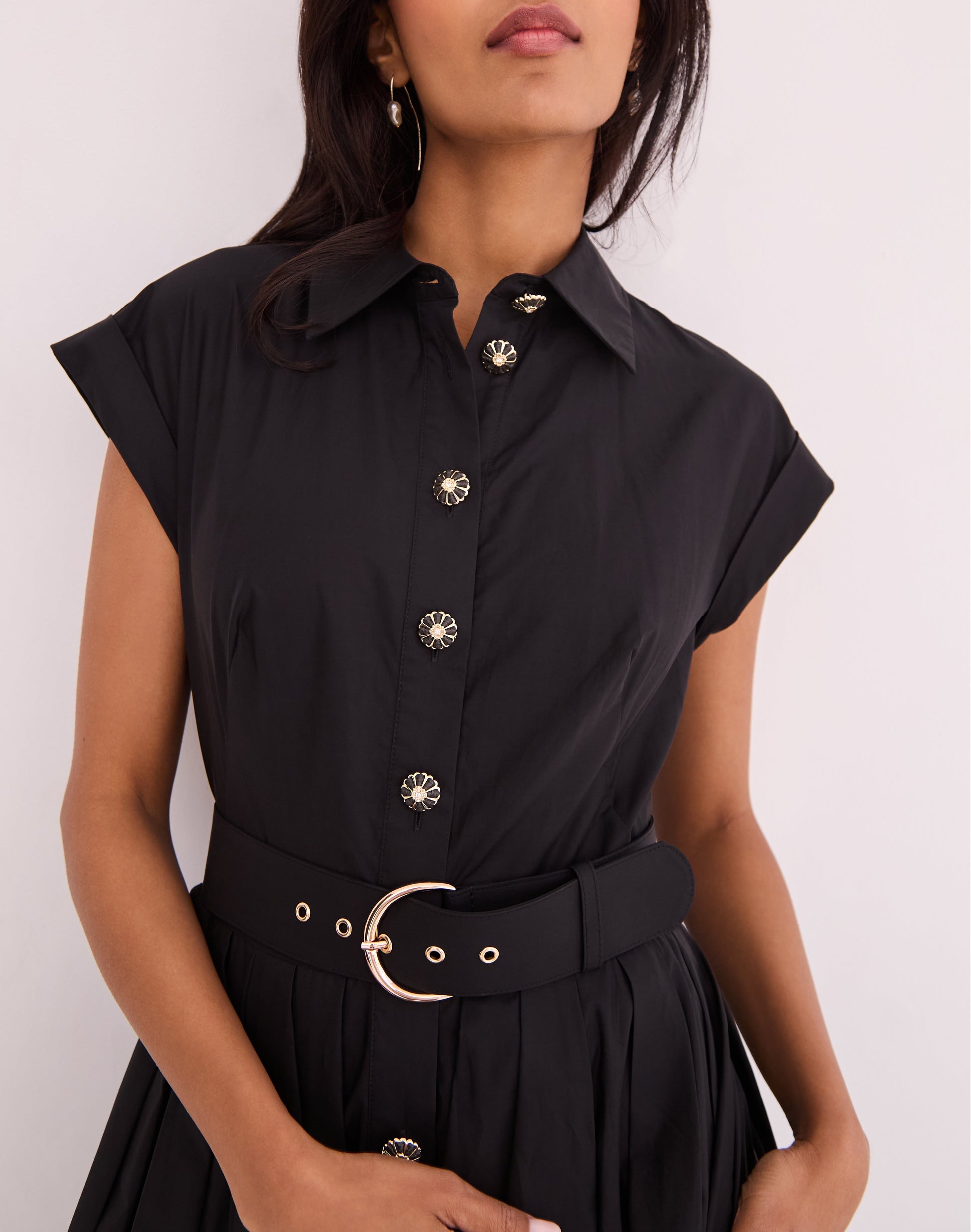 A woman wears the Octavia Dress by Cara Cara—a black belted shirtdress with short sleeves, decorative buttons, and a matching black belt with metallic buckle.