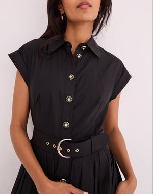 A woman wears the Octavia Dress by Cara Cara—a black belted shirtdress with short sleeves, decorative buttons, and a matching black belt with metallic buckle.