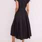 A person shown from the back wears the Octavia Dress by Cara Cara—a short-sleeve, collared, black belted shirtdress with a box pleat skirt—paired with flat sandals.