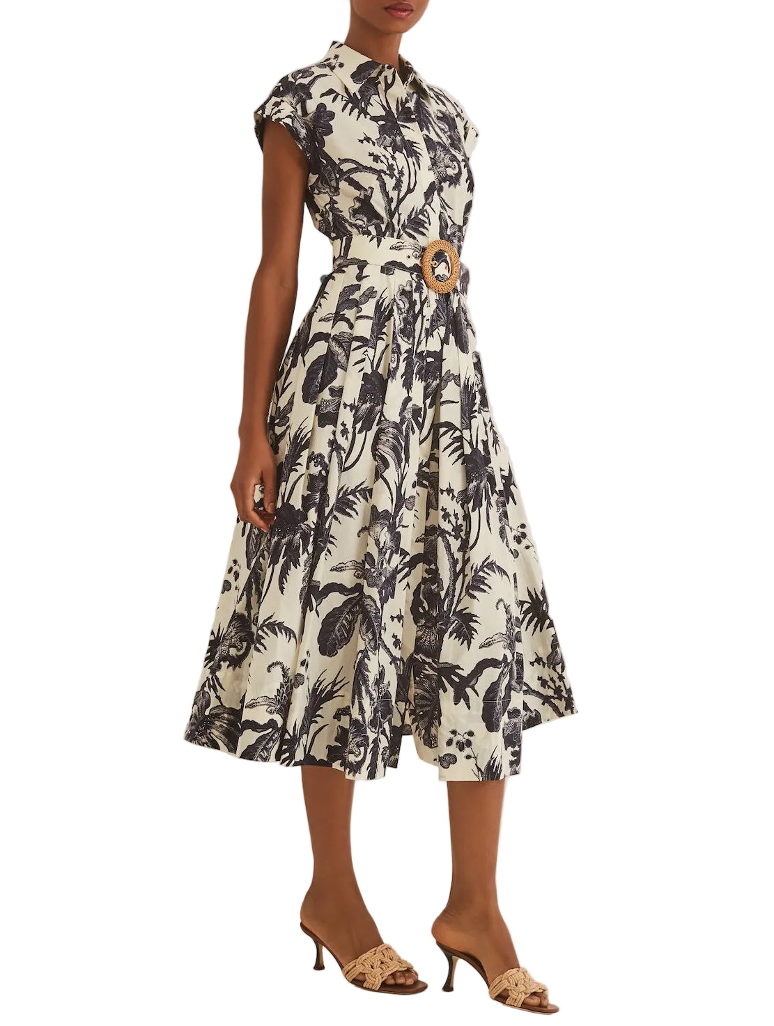 A person wears the Octavia Dress by Cara Cara, featuring a crisp belted silhouette with black palm tree print and short sleeves, paired with tan heeled sandals—a polished, flirtatious look for any occasion.