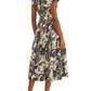 A woman shown from the back wears the Octavia Dress by Cara Cara, featuring a crisp belted design with short sleeves, a collared neckline, and a black-and-white floral midi skirt, paired with beige heeled sandals for a polished look.