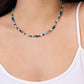 A woman wearing the Milos Beaded Necklace by Anabel Aram, a delicate multicolored piece with lapis lazuli and turquoise beads, paired with a white tank top.