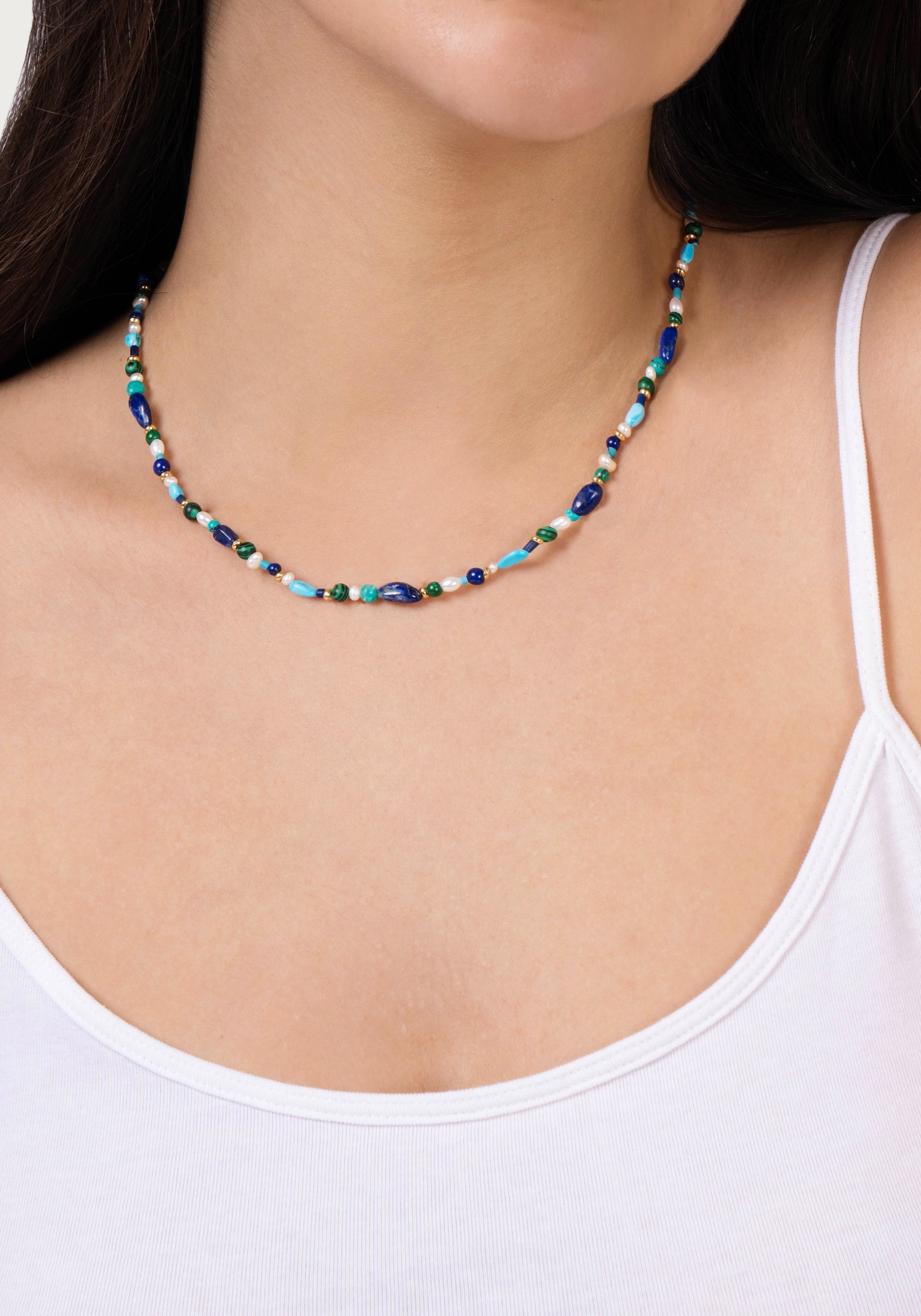A woman wearing the Milos Beaded Necklace by Anabel Aram, a delicate multicolored piece with lapis lazuli and turquoise beads, paired with a white tank top.