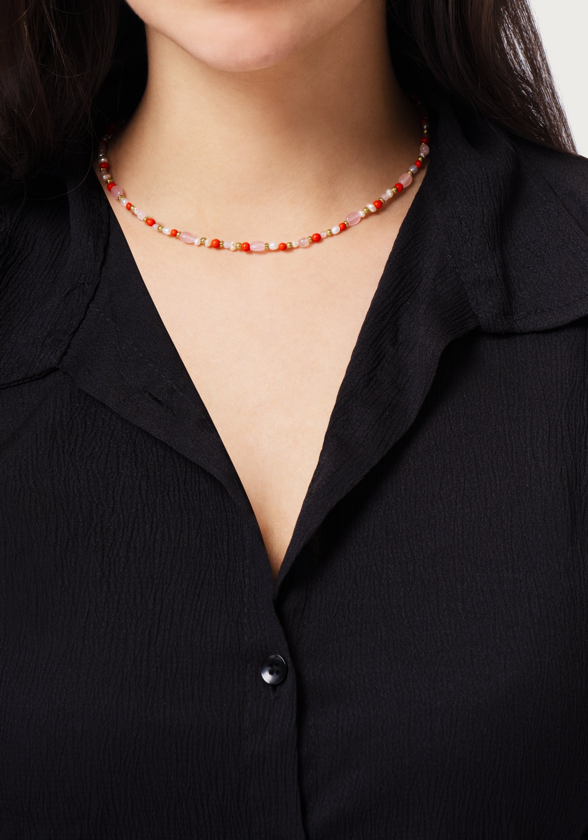 A woman wearing a black textured button-up shirt and the Milos Beaded Necklace by Anabel Aram, featuring red, white, and turquoise beads.