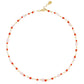 The Milos Beaded Necklace by Anabel Aram features alternating small red, pink, white, and turquoise beads with a gold clasp and adjustable extender.