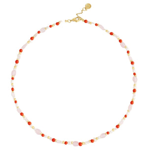 The Milos Beaded Necklace by Anabel Aram features alternating small red, pink, white, and turquoise beads with a gold clasp and adjustable extender.