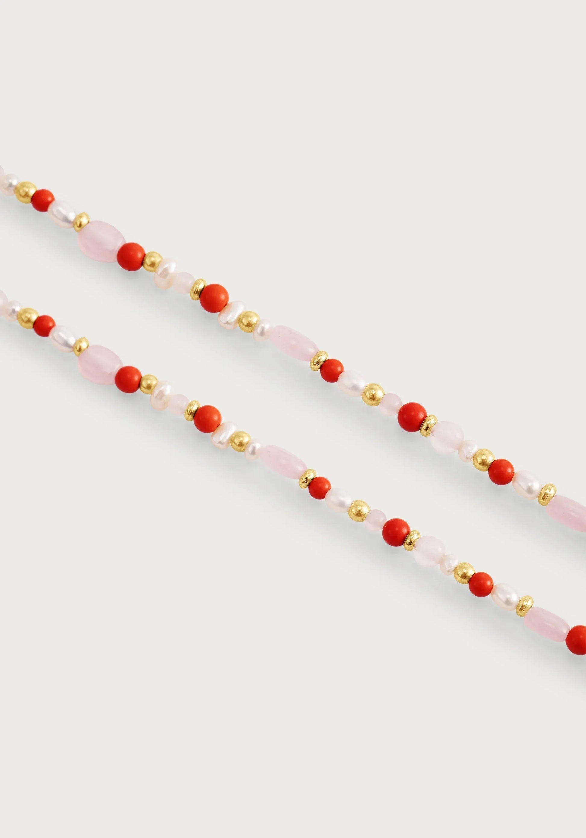 The Milos Beaded Necklace by Anabel Aram features alternating pink, red, white, gold, and turquoise beads, shown against a plain white background.
