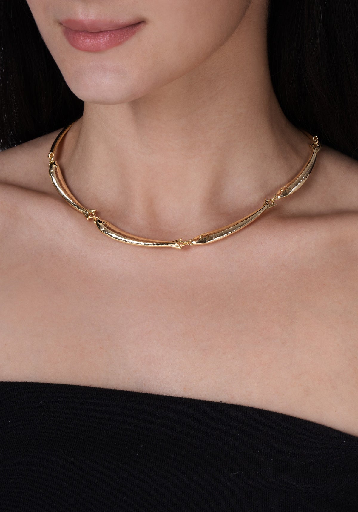 The Milos Fish Necklace is an 18K gold plated statement necklace featuring a series of thin, curved metal links.
