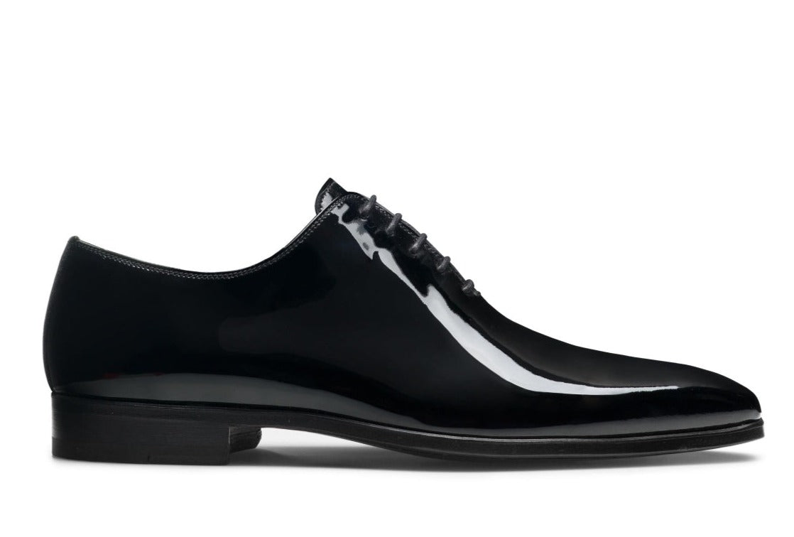 The Magnanni Cruz II Tux Shoes from the Magnanni Core Collection are black patent leather dress shoes designed with a sleek profile, perfect for formal attire. They feature a low heel and lace-up closure.