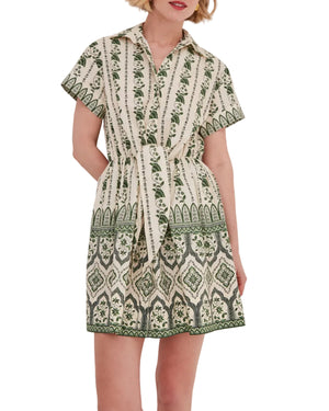 A woman wears the Cara Cara Asbury Mini Dress, a green and cream shirtdress with a placed print, short sleeves, collared button-down front, and matching tie waist.