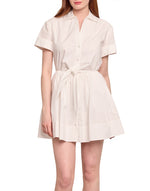 A woman wears the Cara Cara Asbury Mini Dress— a short-sleeved, collared white shirtdress with button-up front and waist tie—while standing against a plain white background.